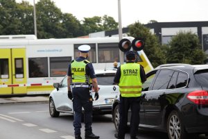 policjant i funkcjonariusz SOK rozdają ulotki, w tle pociąg