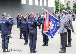 policjanci w mundurach stoją przed sztandarem