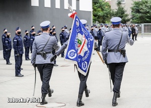 policjanci w mundurach galowych niosą sztandar