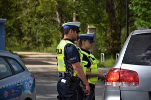 policjant i policjantka stoją przy samochodzie, dokonują kontroli drogowej