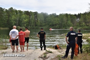 policjanci, strażacy i ratownicy stają przy zbiorniku wodnym