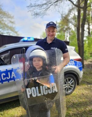 policjant z dzieckiem przymierzają tarczę i kask policyjny